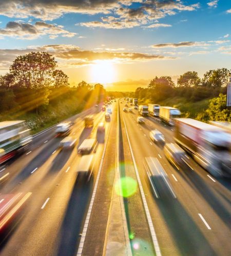 Traffico intenso in movimento a velocità sostenuta su un'autostrada inglese al tramonto.